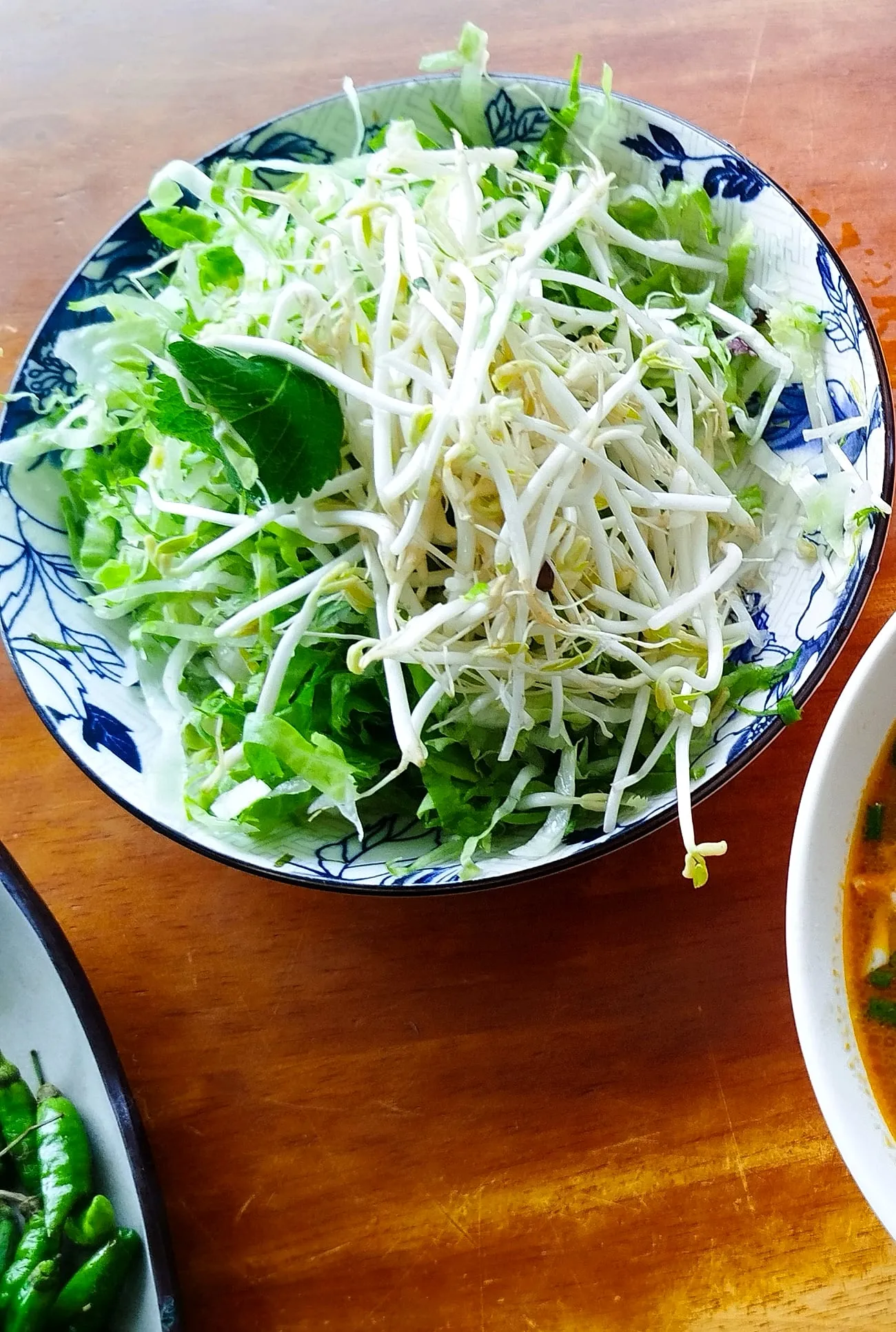 A plate of fresh herbs, bean sprouts and shredded greens served alongside